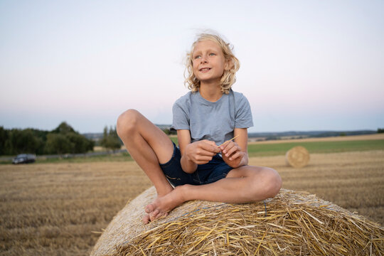 Smiling boy with blond hair sitting on haystack
