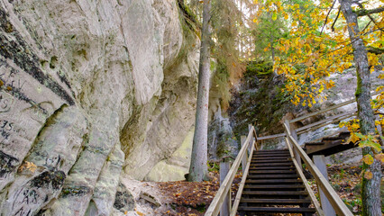 The large sandstone cliffs of Sietiniezis on the banks of the Gauja River in Latvia. tourist nature trail for hiking with wooden stairs. Gauja National Park in the vicinity of Valmiera, Autumn,  - obrazy, fototapety, plakaty