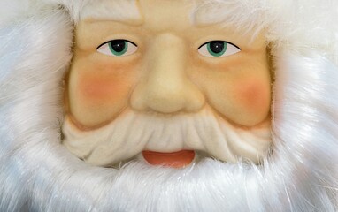 Santa Claus decorative doll closeup with facial features and details, looking at camera. Framed by white beard and hair.