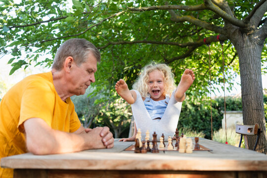 Happy girl enjoying by grandfather playing chess on table in garden