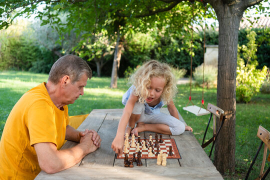 Granddaughter playing chess with grandfather in garden