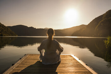 Woman meditating on jetty over lake at vacation