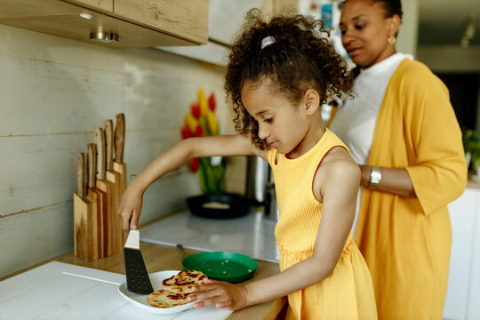 Girl Helping Mother In Cooking At Kitchen Counter