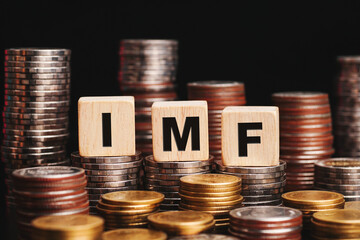 Stacks of gold coins with the letters IMF (International Monetary Fund) on a wooden cube. Business concept.