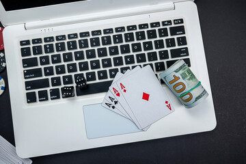 two black gambling dice lie with twisted dollar bills and cards on a laptop keyboard.