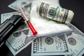 Packages of powdered substances and dollar bills next to a gun and a medical syringe.