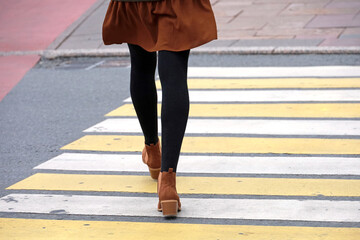 Naklejka premium Female legs in black warm tights and brown shoes on pedestrian crossing. Slim girl walking on a street, fashion in autumn city