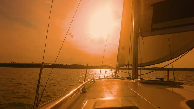 Sail boat with set up sails gliding in open sea at sunset