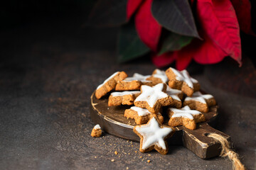 Typical Christmas treat. Star shape ginger cookies with sugar icing on woode try with poinsettia flower on cocnrete background. Copy space.