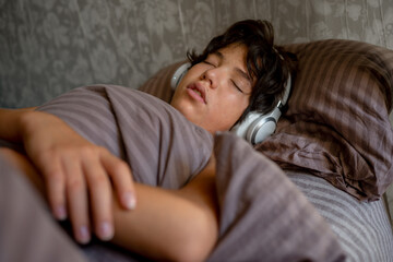 teenage boy sleeps at home on the couch listening to music with headphones