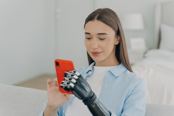 Happy disabled young girl with bionic arm prosthesis holding smartphone, shopping in online store