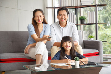 Happy Asian family lifestyle enjoy watching TV in living room at home. Happy Asian family portrait with mother, father and daughter while writting note.