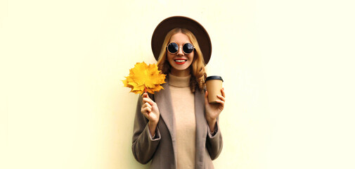 Autumn portrait of beautiful smiling young woman with yellow maple leaves wearing round hat, coat on white background