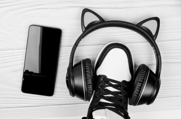 Sneakers with wireless headphones and smartphone on white wooden background