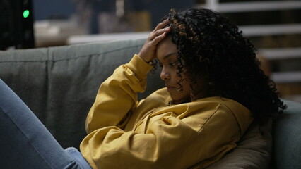One upset young black woman feeling frustration. An anxious African American girl laid on sofa in...
