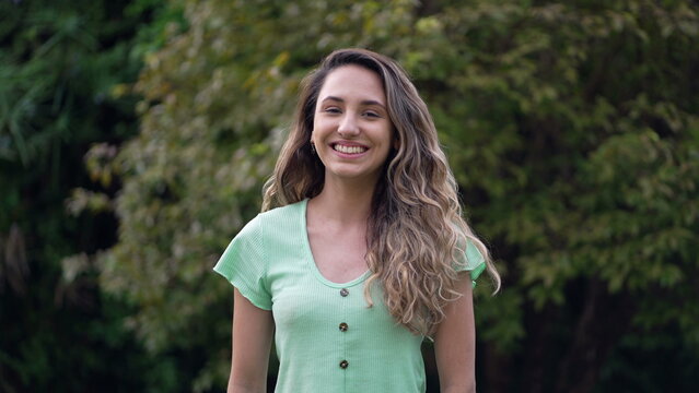 One Happy Young Hispanic Woman Standing Outdoors Smiling At Camera. Portrait Of A Casual Female South American Person Closeup Face