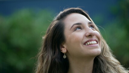 Fototapeta premium Happy young millennial woman staring at sky smiling in contemplation. Calm girl looks up headshot