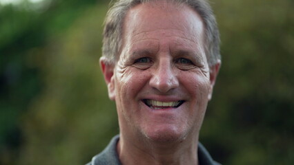 Happy middle aged man standing at park looking at camera. Portrait of an older male person closeup face