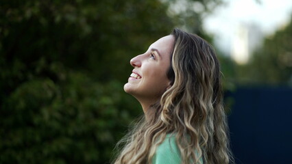 Naklejka premium Happy hopeful young millennial woman standing outside smiling looking at sky with FAITH