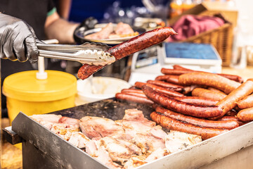 Street vendor holds large sausage by pliers during a sale at the street food fair