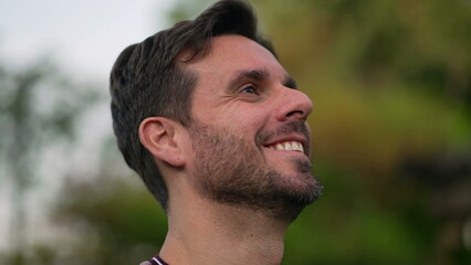 Fototapeta premium Spiritual man closing eyes in contemplation outdoors. Carefree person opening eye looking up at sky smiling with HOPE and FAITH. Grateful emotion