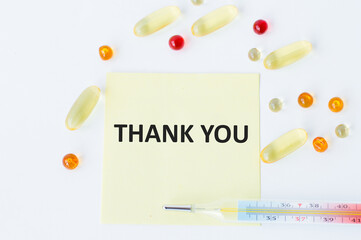 Thank you text on a yellow card on a white background next to scattered tablets