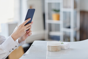 Minimal closeup of young woman taking product images of handmade beauty creams and SPA salts with smartphone