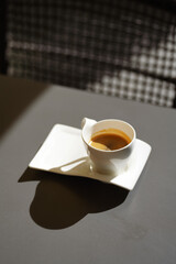 Drinking coffee on a terrace in direct sunlight. Close up photo with a white ceramic cup of a fresh espresso.