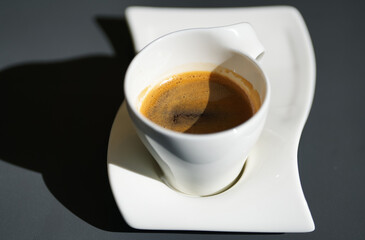 Drinking coffee on a terrace in direct sunlight. Close up photo with a white ceramic cup of a fresh espresso.