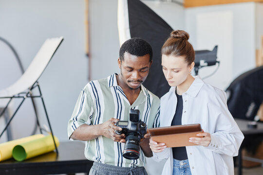 Waist up portrait of two young photographers looking at pictures in camera in studio setting