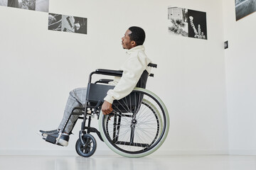 Side view portrait of black young man using wheelchair while visiting modern art gallery, copy space