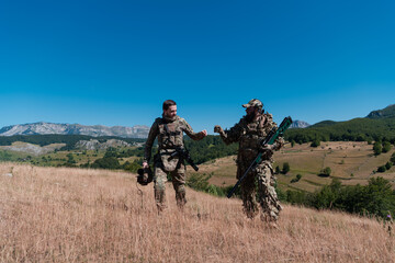 A sniper team squad of soldiers is going undercover. Sniper assistant and team leader walking and aiming in nature with yellow grass and blue sky. Tactical camouflage uniform.