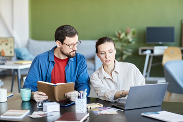 Young confident businesswoman explaining her colleague online information while both watching video training by workplace