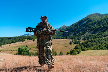 army soldier holding a sniper rifle with scope and walking in the forest. war, army, technology and...