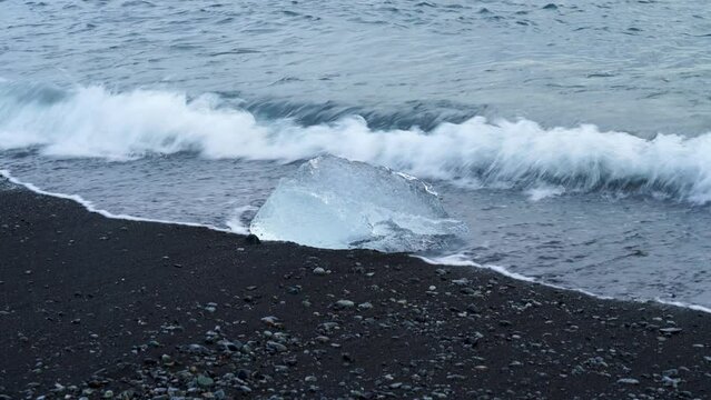 Slow Motion of Ocean Wave Flooding Ice Cube on black beach shore in Iceland