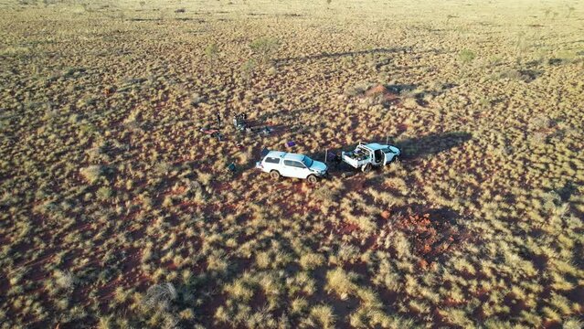 Reversing and rising aerial footage of two cars and people packing up camp in the Tanami Desert, Northern Territory, Australia. August 2022.
