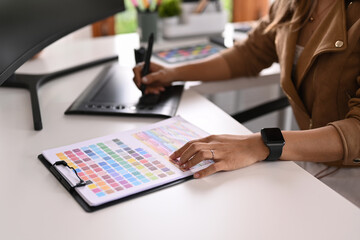 Cropped shot of creative woman working with color palette and graphic tablet on white table