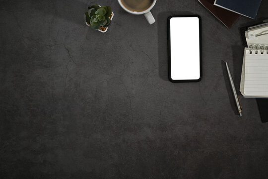 Smart phone with blank screen, notepad and coffee cup on black background. Flat lay, Top view with copy space
