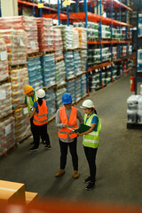 Overhead view of male manager and worker discussing work while walking in aisle between rows of tall shelves full of packed boxes