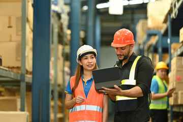 Male managers and worker checking newly arrived goods on digital tablet while standing near tall shelves in large warehouse