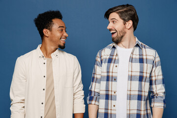 Young two friends shocked cheerful men 20s wear white casual shirts looking camera together look to each other with open mouth isolated plain dark royal navy blue background. People lifestyle concept.