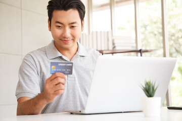 Happy cheerful smiling young adult asian man doing online shopping or e-shopping satisfied entrepreneur making online payment paying for service or goods.