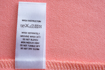 White laundry care washing instructions clothes label on pink cotton shirt