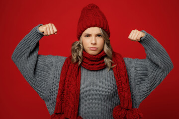 Young woman wear warm gray sweater scarf hat show biceps muscles on hand demonstrating strength...