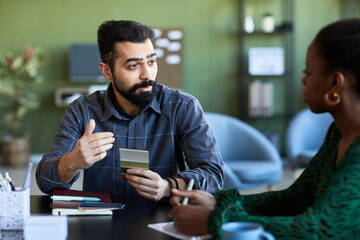 Confident bearded businessman with color swatches explaining something to African American female colleague at meeting