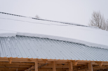 snow sliding down from roof. building construction house with metal roof covered fresh icy frozen...