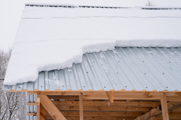 snow sliding down from roof. building construction house with metal roof covered fresh icy frozen snow and snowflakes on frosty winter day in country village suburb. snowy winter season. cold weather