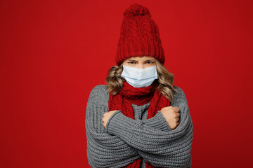 Young frozen sad woman wear grey sweater scarf hat sterile mask hold warm herself isolated on plain...