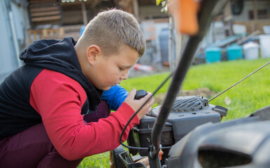 the boy is mowing the grass. He opened the lawnmower tank, holds the tank cap in his hand and checks how much fuel is left