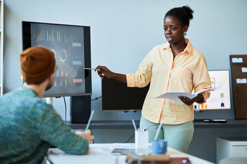 Confident coach pointing at interactive screen with graphic data at seminar while making presentation and explaining it